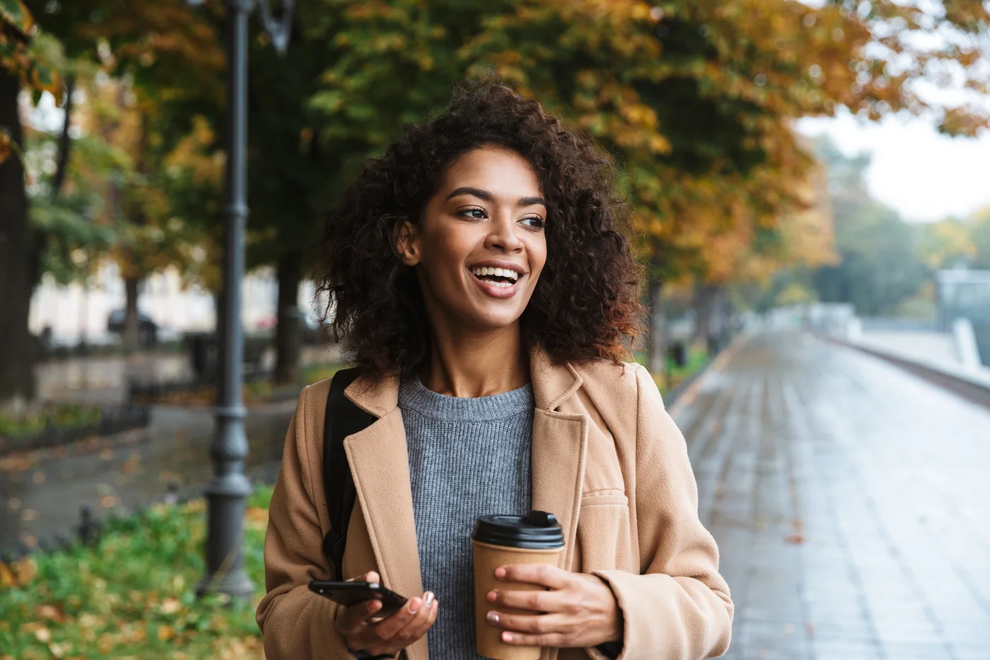 A smiling employee walking through a tree-lined park in autumn